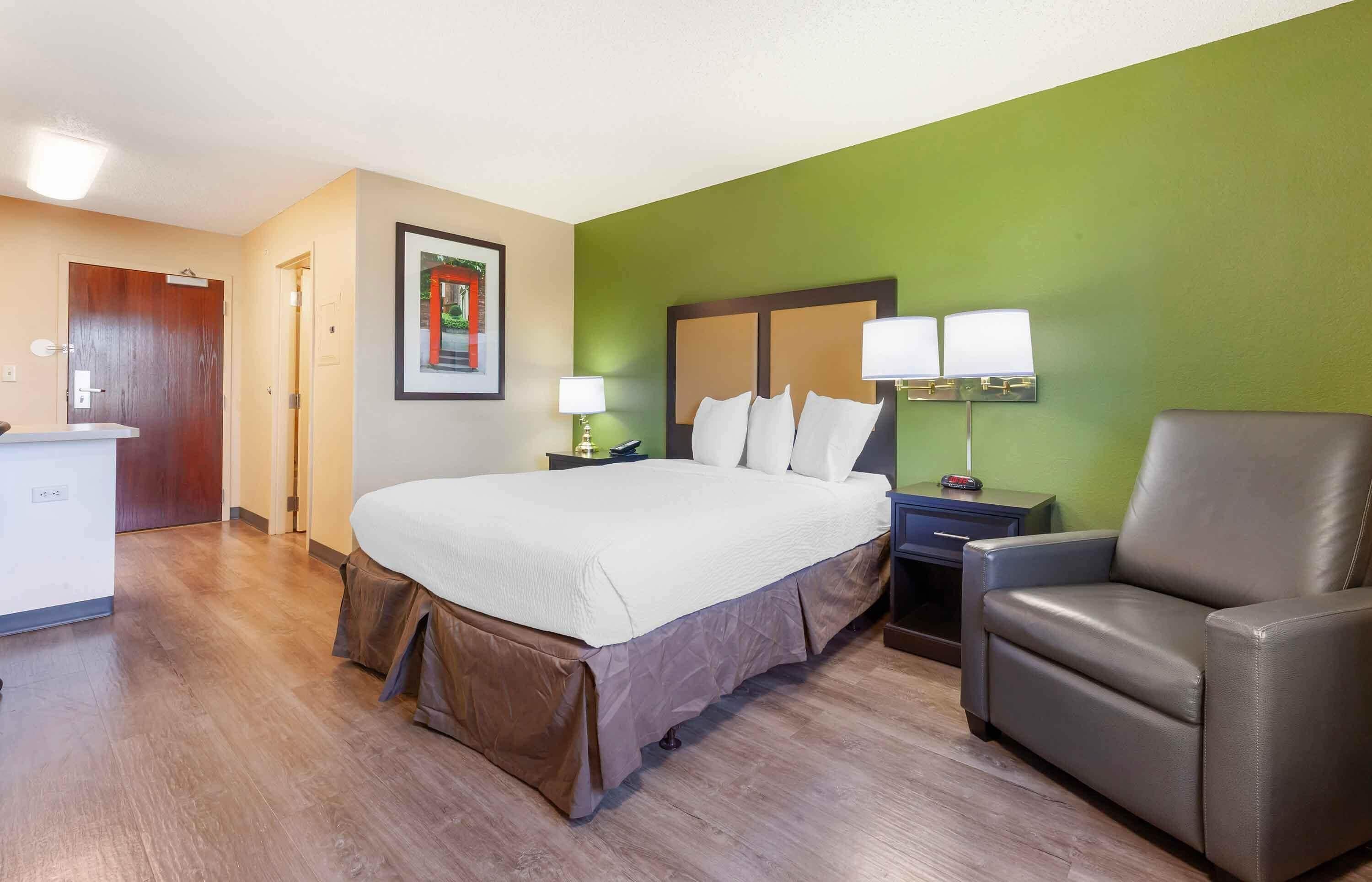 A hotel room with a bed, a desk, a chair, and a nightstand with lamps.