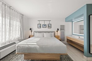A modern bedroom with a large bed, bedside tables with lamps, a built-in wardrobe, and a large mirror.