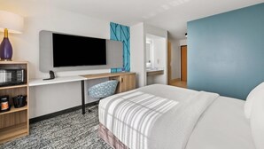 Una habitación de hotel moderna con una cama grande, un escritorio con televisor de pantalla plana, un microondas y una cafetera.