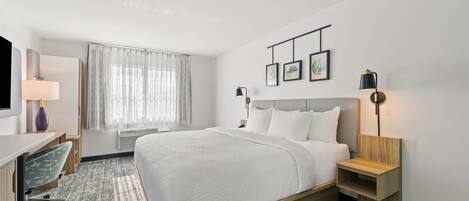 Quarto de hotel com cama, mesas de cabeceira, escrivaninha, cadeira, televisão e janela com cortinas.