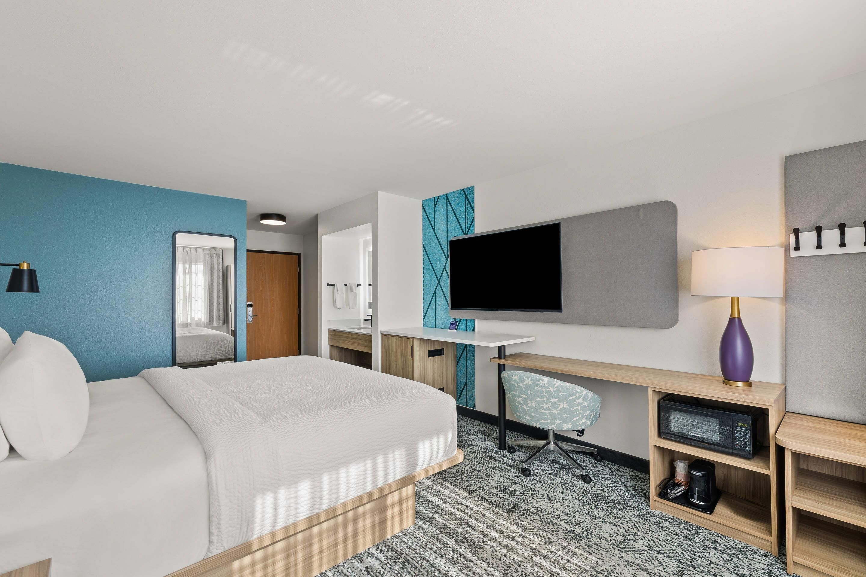 Una habitación de hotel moderna con una cama grande, un escritorio, un televisor y una silla.