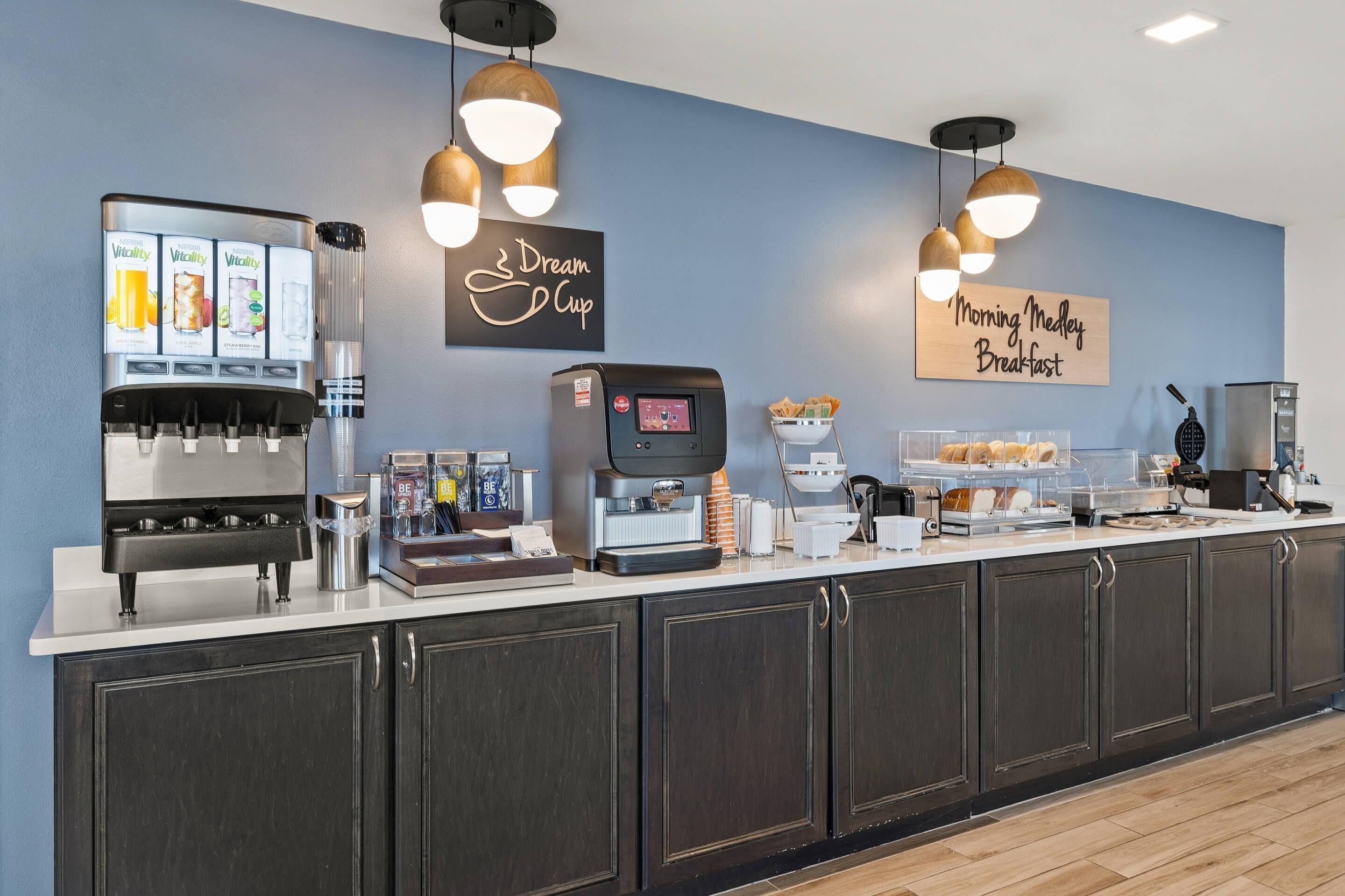 A breakfast bar with a coffee machine, a juice dispenser, and a sign that reads 'Dream Cup.'