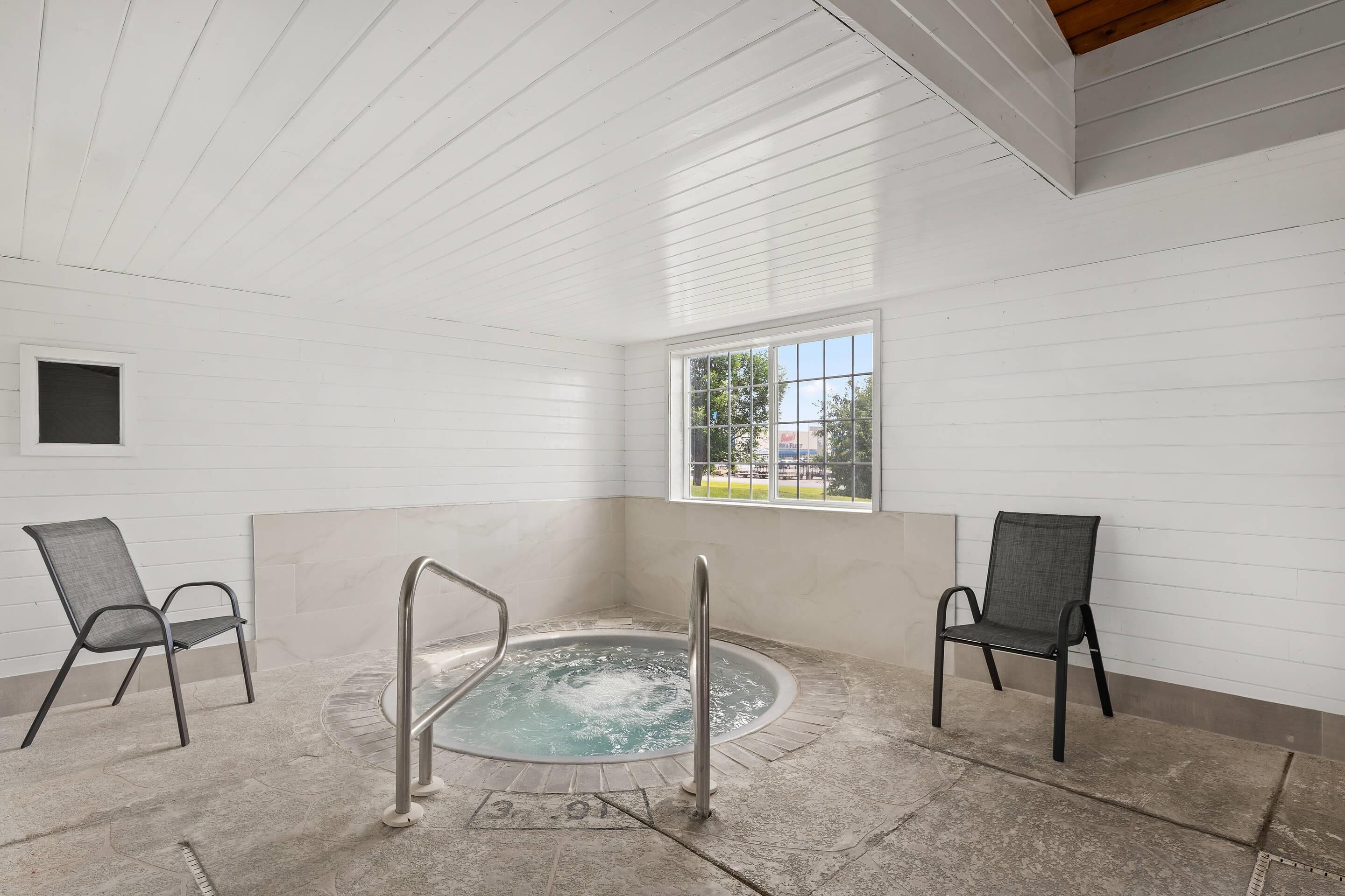 A spa room with a hot tub, two chairs, a window, and a tiled floor.