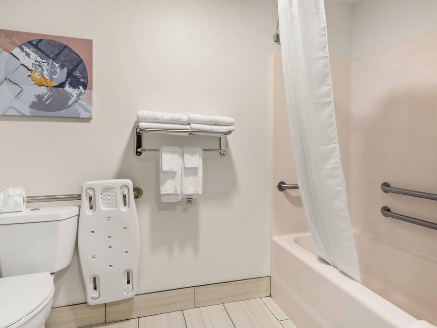 Un baño con inodoro, ducha con cortina, toallero con toallas y dispensador de papel higiénico en la pared.