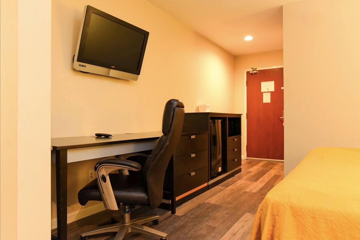 Una camera d'albergo con scrivania, sedia, televisione, armadio e letto.