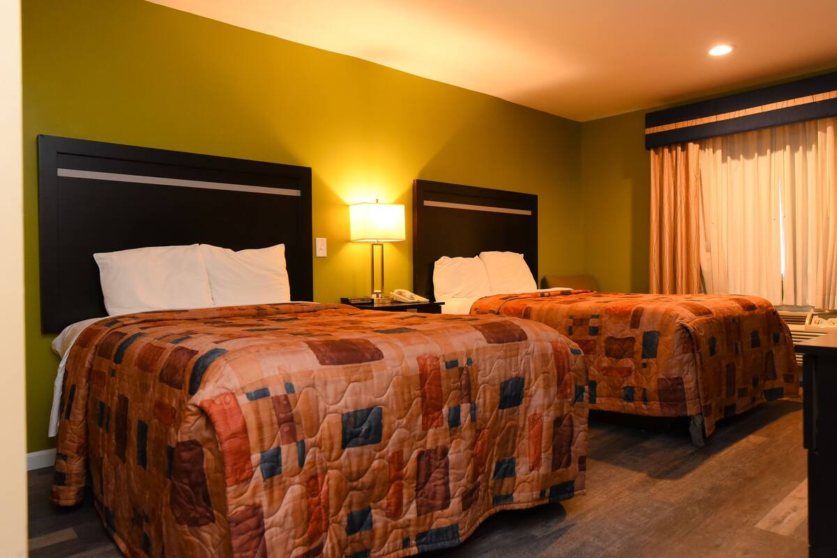 Una camera d'albergo con due letti, un comodino con una lampada e una finestra con tende.