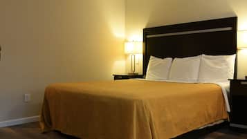 A neatly made bed with a brown bedspread, two white pillows, and a dark headboard. There are two bedside lamps with white shades, and a wall-mounted light fixture. The room has wooden flooring and beige walls.