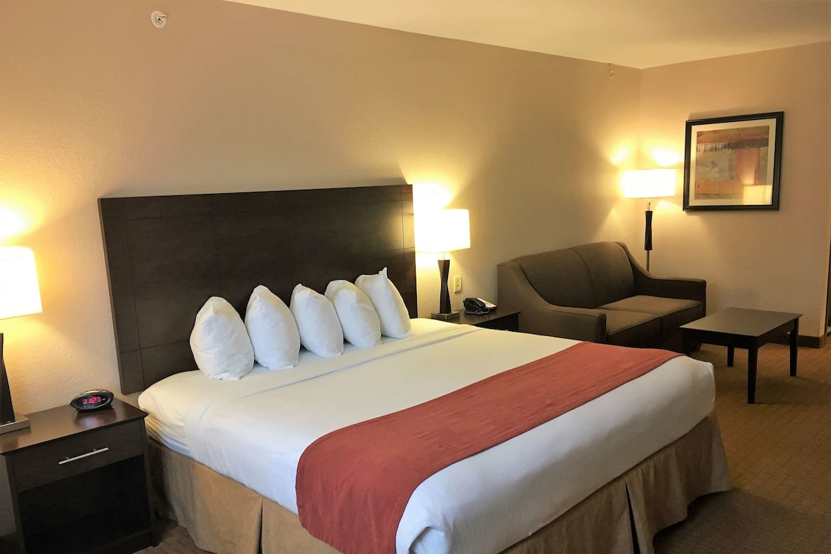 A hotel room with a large bed, two bedside lamps, a chair, a small table, and a painting on the wall.