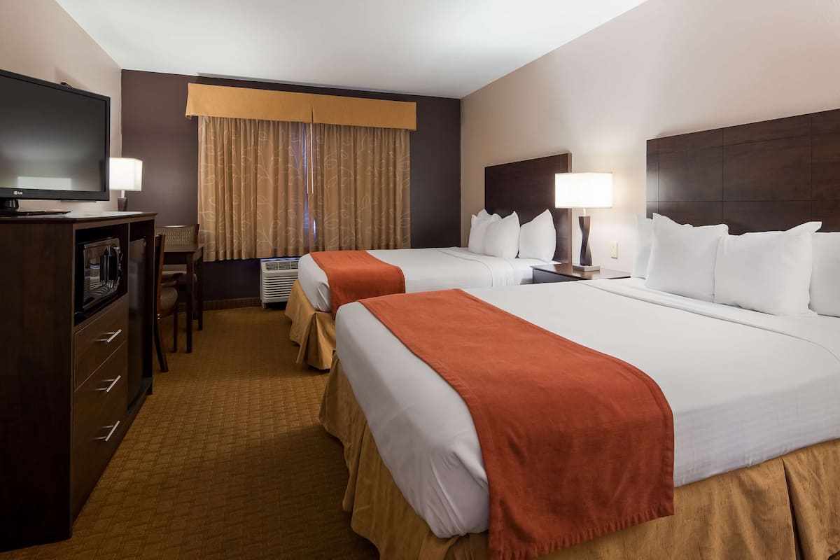 A hotel room with two beds, a desk, a TV, and a window with curtains.
