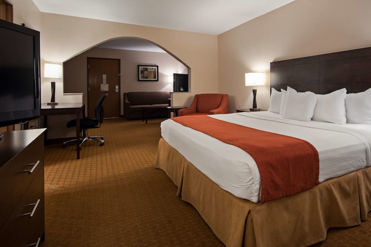 A hotel room with a large bed, a desk, a chair, a TV, and a sofa.