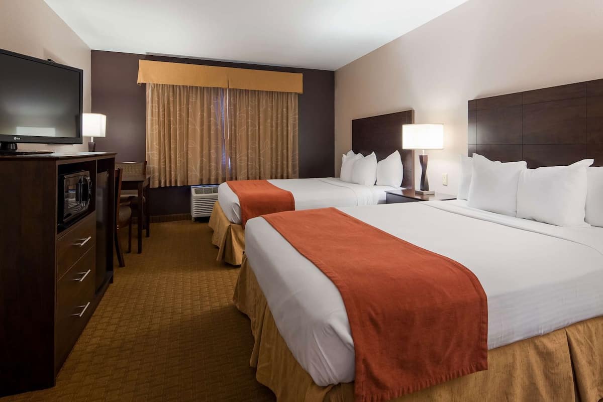 A hotel room with two beds, a desk, a television, and a window with curtains.