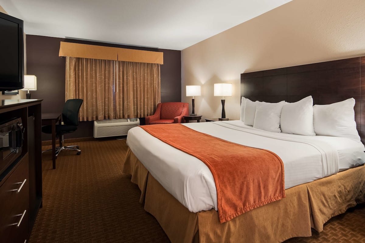 A hotel room with a large bed, two bedside tables, a desk with a television, a chair, and a window with curtains.