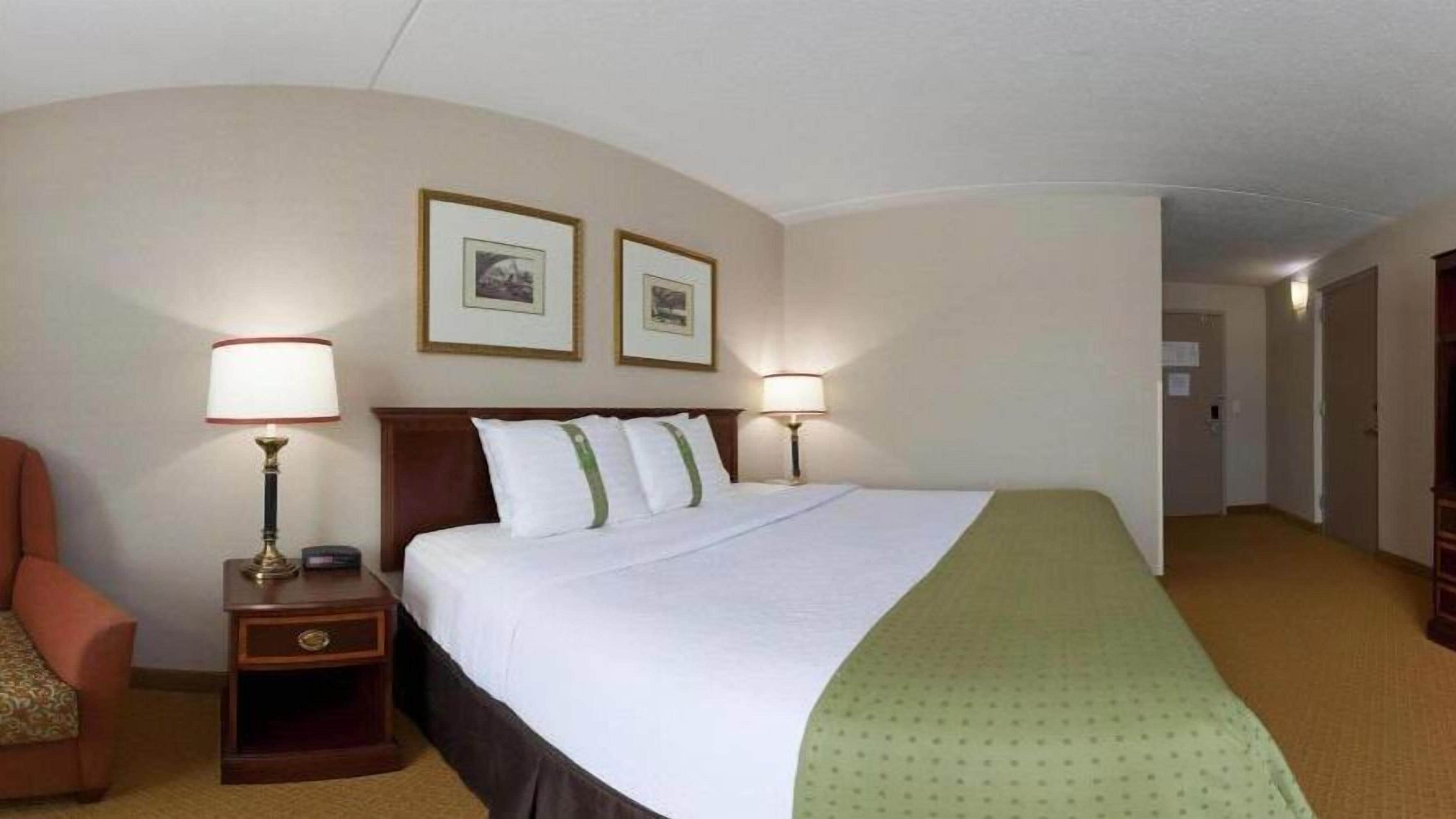 A hotel room with a large bed, two bedside lamps, a nightstand, a chair, and two framed pictures on the wall.