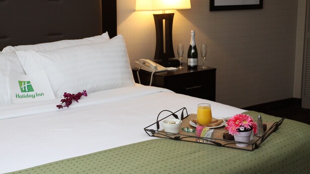 A hotel room with a neatly made bed, a bedside table with a lamp, a tray with breakfast items, and a framed picture on the wall. - Holiday Inn Budd Lake - Rockaway Area by IHG (Budd Lake)
