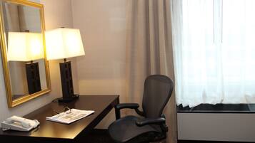 A hotel room with a desk, two lamps, a chair, a telephone, and a window with curtains.