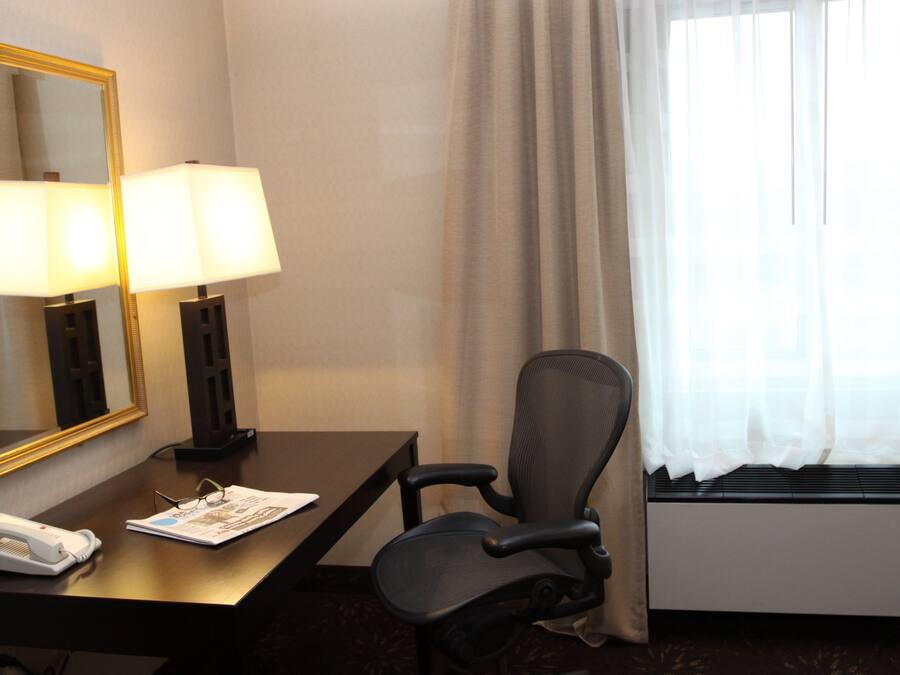 A hotel room with a desk, two lamps, a chair, a telephone, and a window with curtains.