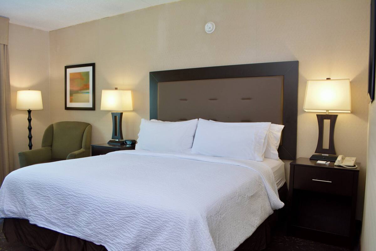 A hotel room with a large bed, two bedside tables, a chair, and two lamps.