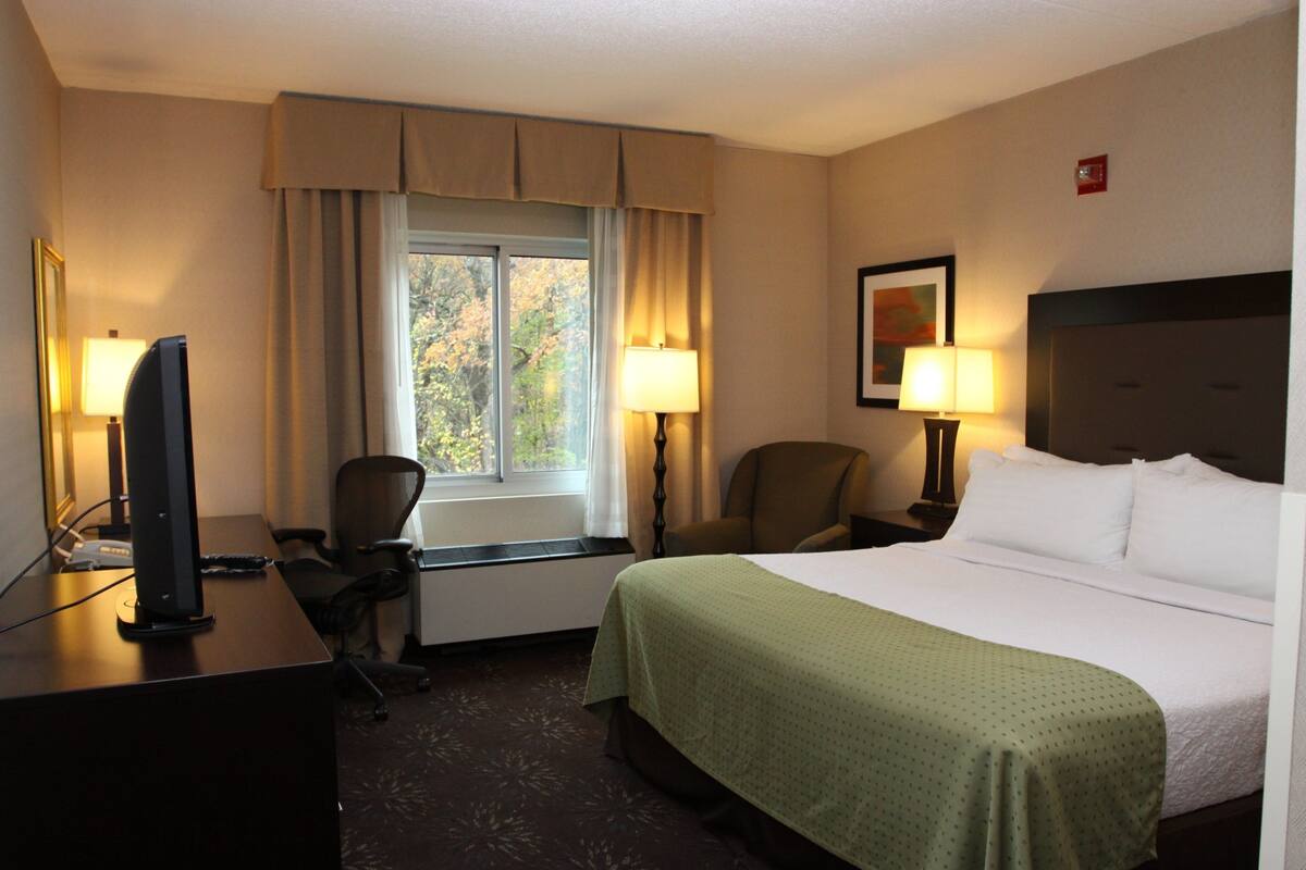 A hotel room with a bed, desk, chair, and two lamps.