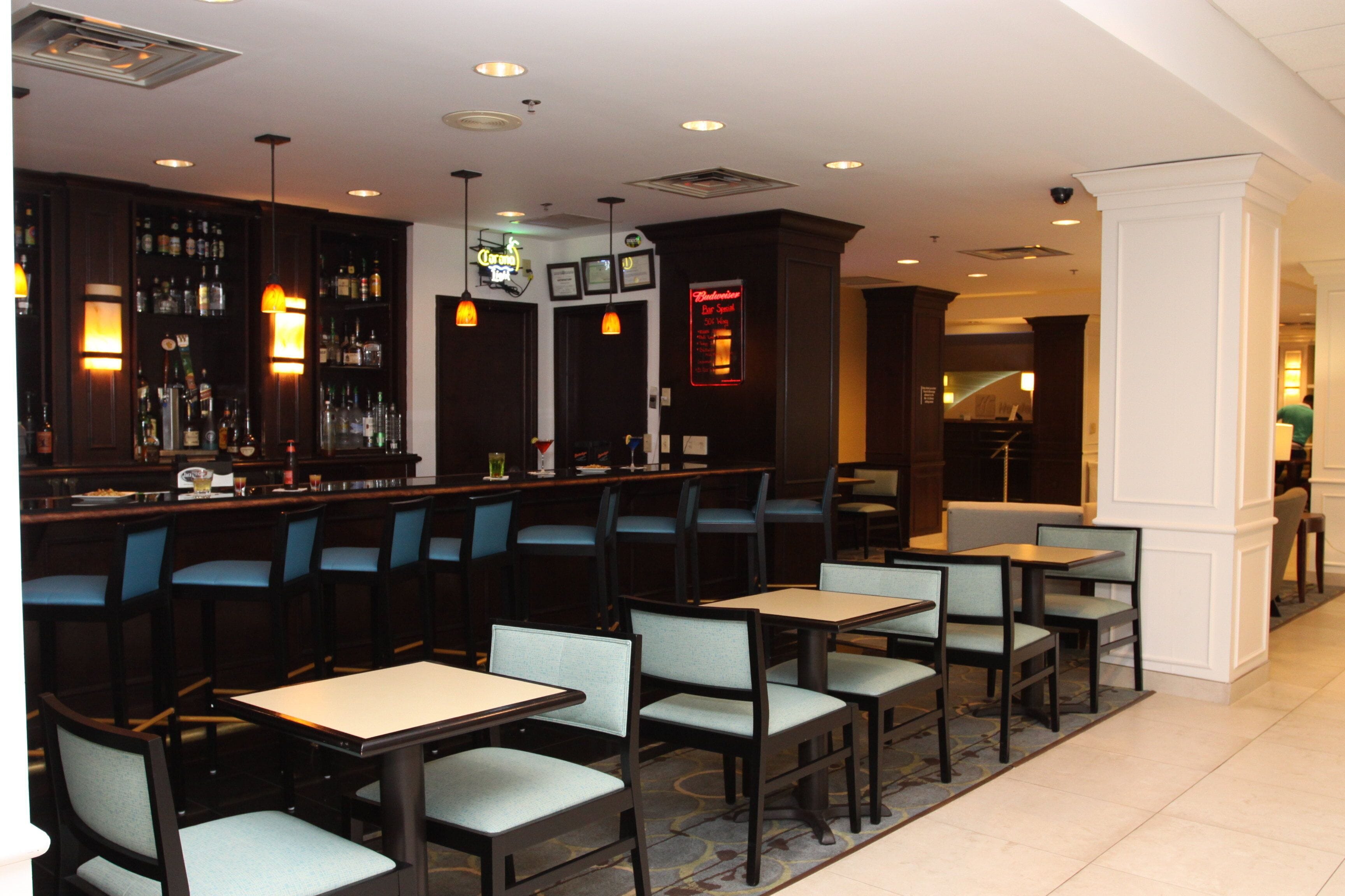 A restaurant with a bar area, multiple tables and chairs, and a variety of lighting fixtures.