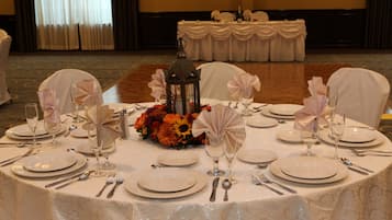 Mesa redonda dispuesta para un evento formal, con mantel blanco, platos, cubiertos y cristalería.