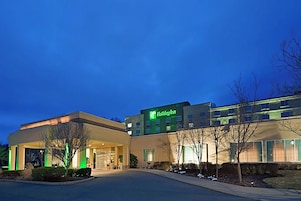 Un hotel Holiday Inn con un diseño moderno, que cuenta con una entrada bien iluminada y un área de estacionamiento.