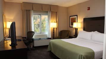 Ein Hotelzimmer mit Bett, Schreibtisch, Stuhl, zwei Lampen, Fernseher und einem fenster mit Vorhängen.