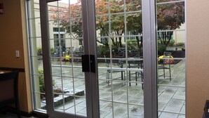 A view through a glass door into an outdoor patio area with tables and chairs, a fire hydrant, and trees with pink foliage. - Holiday Inn Budd Lake - Rockaway Area by IHG (Budd Lake)