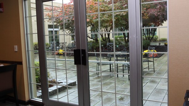 A view through a glass door into an outdoor patio area with tables and chairs, a fire hydrant, and trees with pink foliage. - Holiday Inn Budd Lake - Rockaway Area by IHG (Budd Lake)