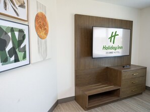 Une chambre d’hôtel Holiday Inn équipée d’un téléviseur à écran plat fixé sur un meuble en bois, d’un petit meuble pour la télévision et d’une œuvre d’art encadrée accrochée au mur.