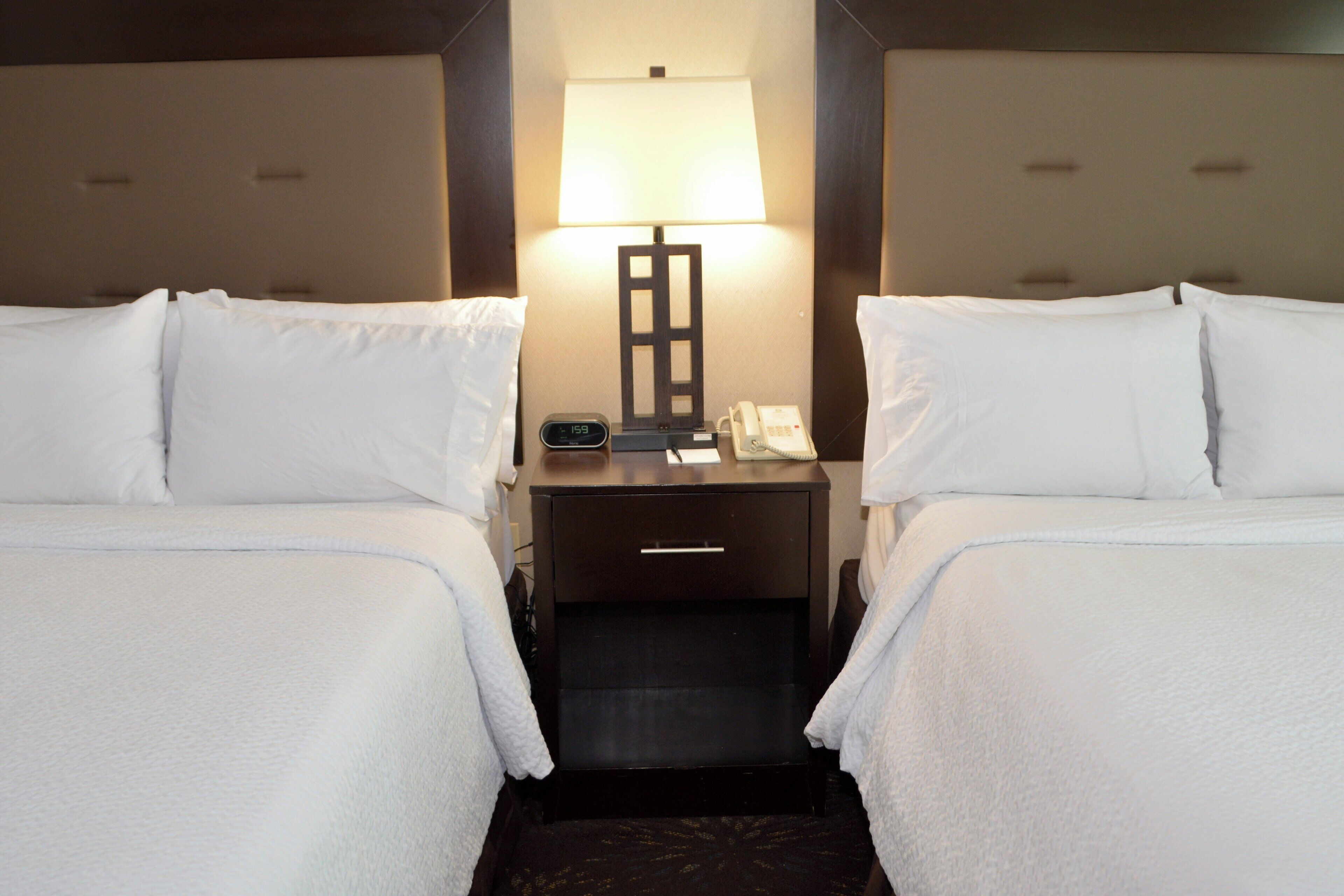 A hotel room with two beds, a nightstand with a lamp, a phone, and a digital clock.