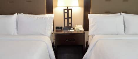 A hotel room with two beds, a nightstand with a lamp, a phone, and a digital clock.