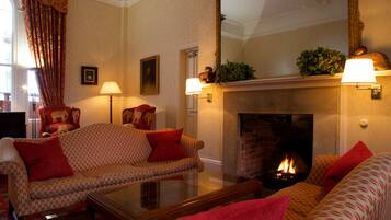 A cozy living room with a fireplace, patterned sofas, and a glass coffee table.