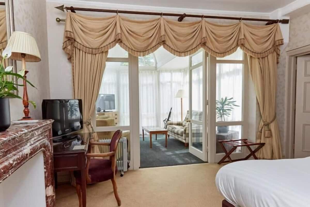 Ein Hotelzimmer mit einem Bett, einem Schreibtisch mit Stuhl, einem Fernseher und Blick durch große Fenster nach draußen.