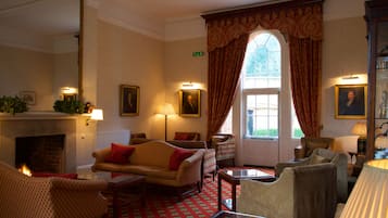 A traditional room with a fireplace, multiple seating options, and a large window with curtains.