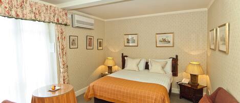 Habitación de hotel con cama, dos mesitas de noche con lámparas, una mesa redonda, un sillón rojo y una ventana con cortinas.