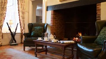A cozy living room with a fireplace, leather armchairs, a coffee table with tea set, and a patterned rug.