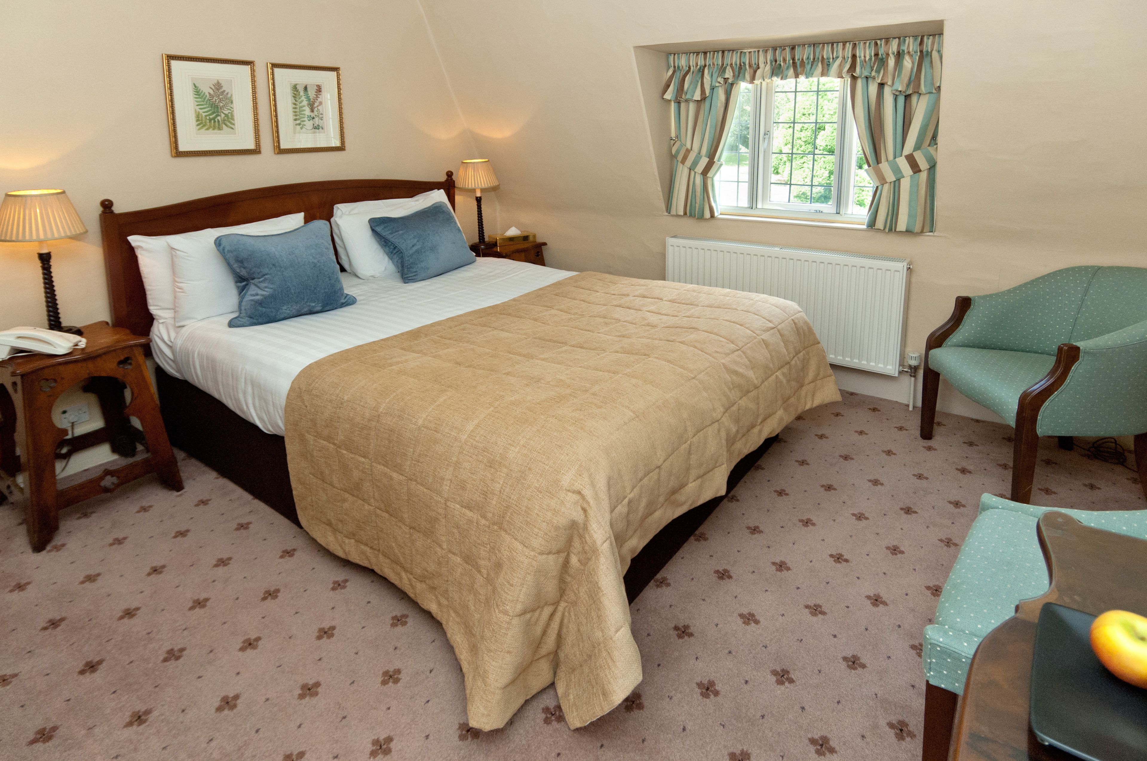 A bedroom with a large bed, two bedside tables, a chair, a radiator, and a window with curtains.