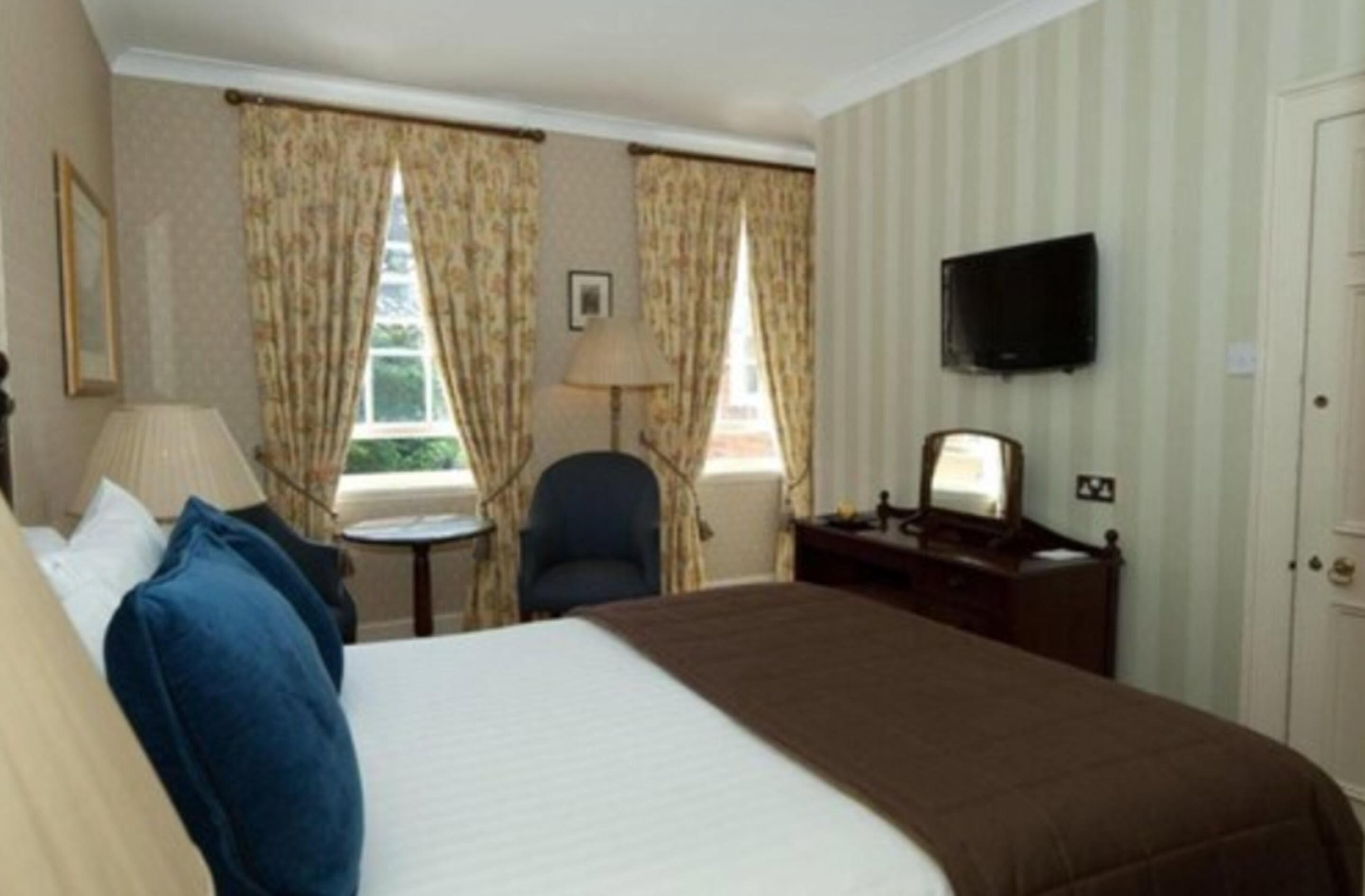 Une chambre d’hôtel avec un lit, un bureau, une chaise, une télévision et des rideaux.