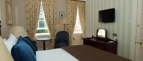 Une chambre d’hôtel avec un lit, un bureau, une chaise, une télévision et des rideaux.