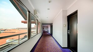 A hotel corridor with a purple carpet, large windows, and a view of buildings with orange roofs. - Jakarta Airport Hotel (Tangerang)