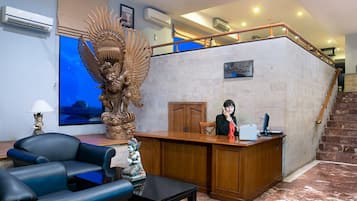 Zona de recepción con mostrador, una estatua decorativa grande, un sofá y una escalera.