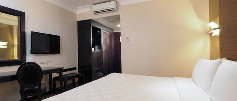 A hotel room with a bed, a desk, a chair, a television, and an air conditioning unit.