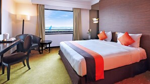 A hotel room with a large bed, a desk, a chair, a small table, and a view of the airport. - Jakarta Airport Hotel (Tangerang)