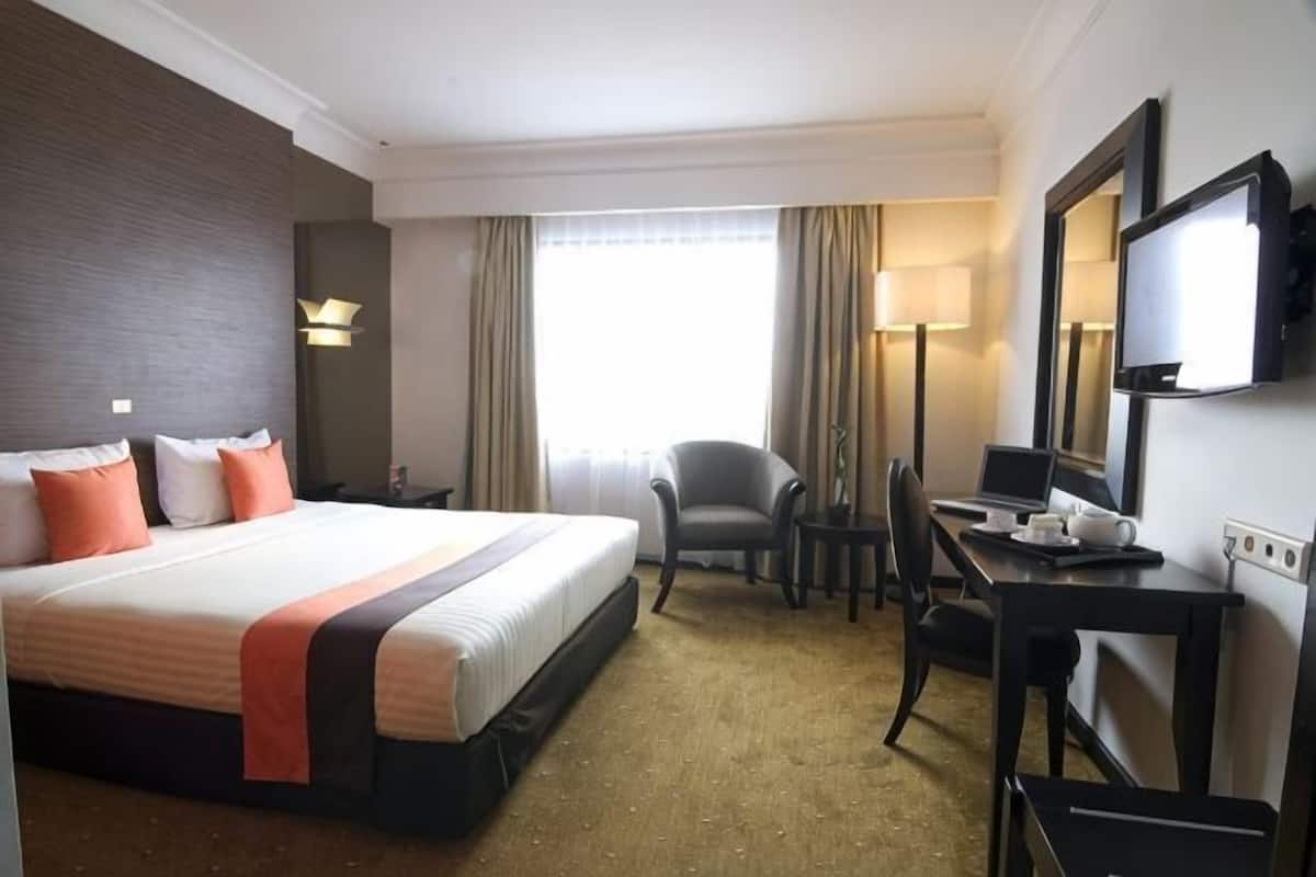 Una habitación de hotel con una cama grande, un escritorio con silla, un televisor y una ventana con cortinas.