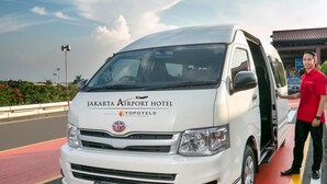 A white van with "Jakarta Airport Hotel" and "Topotels Hotels & Resorts" branding, parked on a road with a person standing beside it. - Jakarta Airport Hotel (Tangerang)