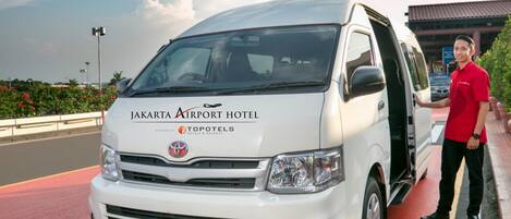 A white van with "Jakarta Airport Hotel" and "Topotels Hotels & Resorts" branding, parked on a road with a person standing beside it.