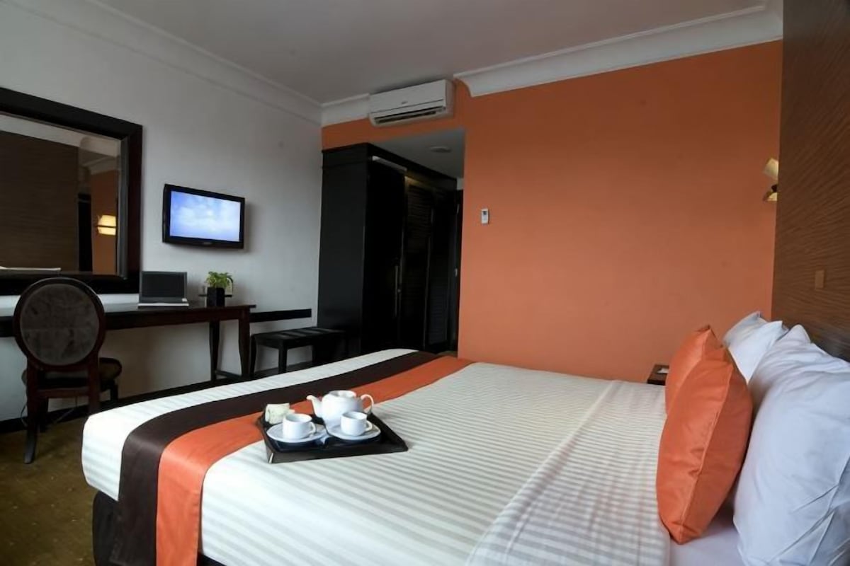 A hotel room with a bed, a desk with a laptop, a television, and a tray with cups and a teapot.