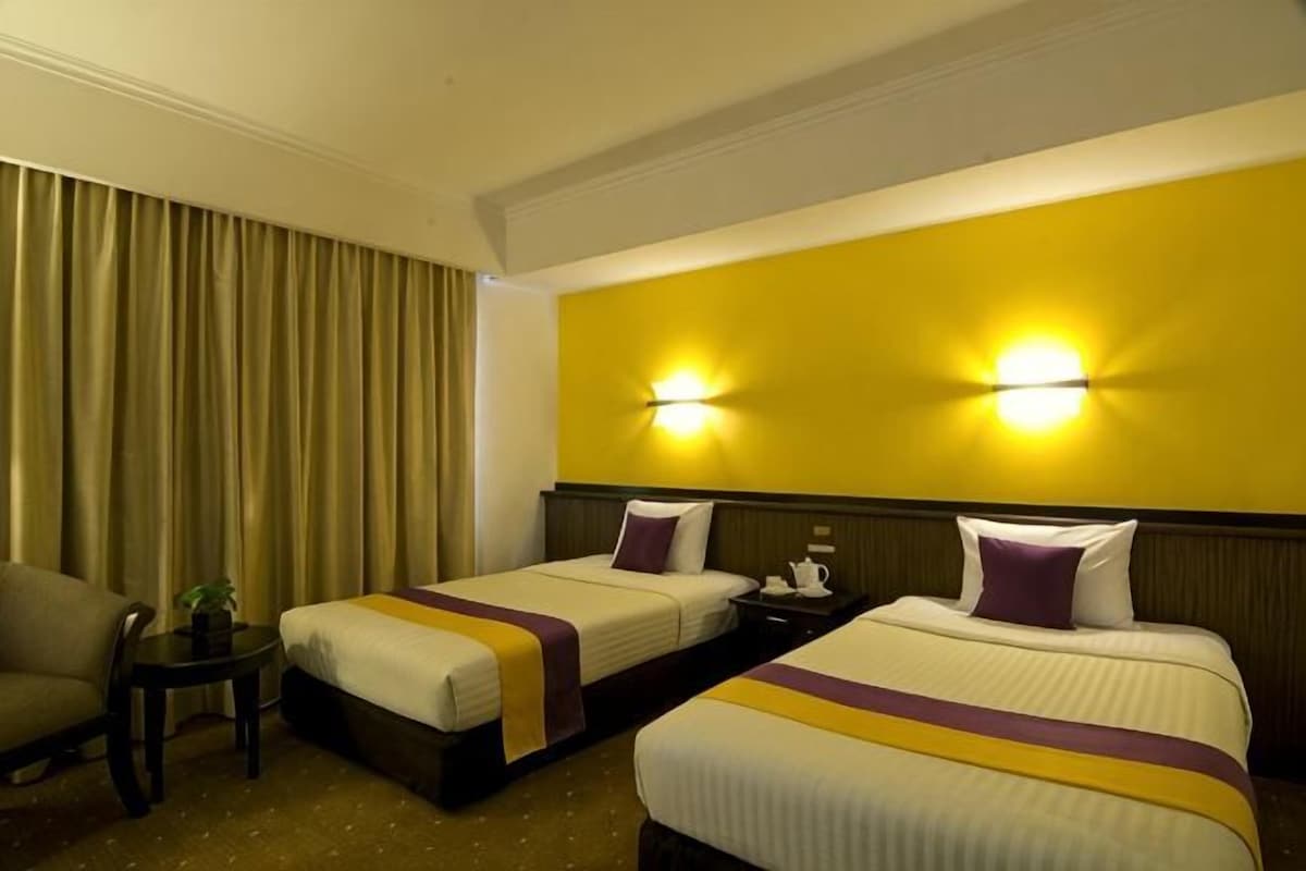 A hotel room with two beds, a nightstand, a chair, and a lamp.