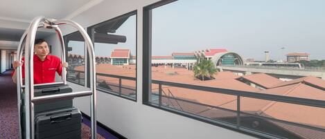 Ein Hotelzimmer mit großem Fenster, Gepäckwagen und Blick auf Flughafengebäude.