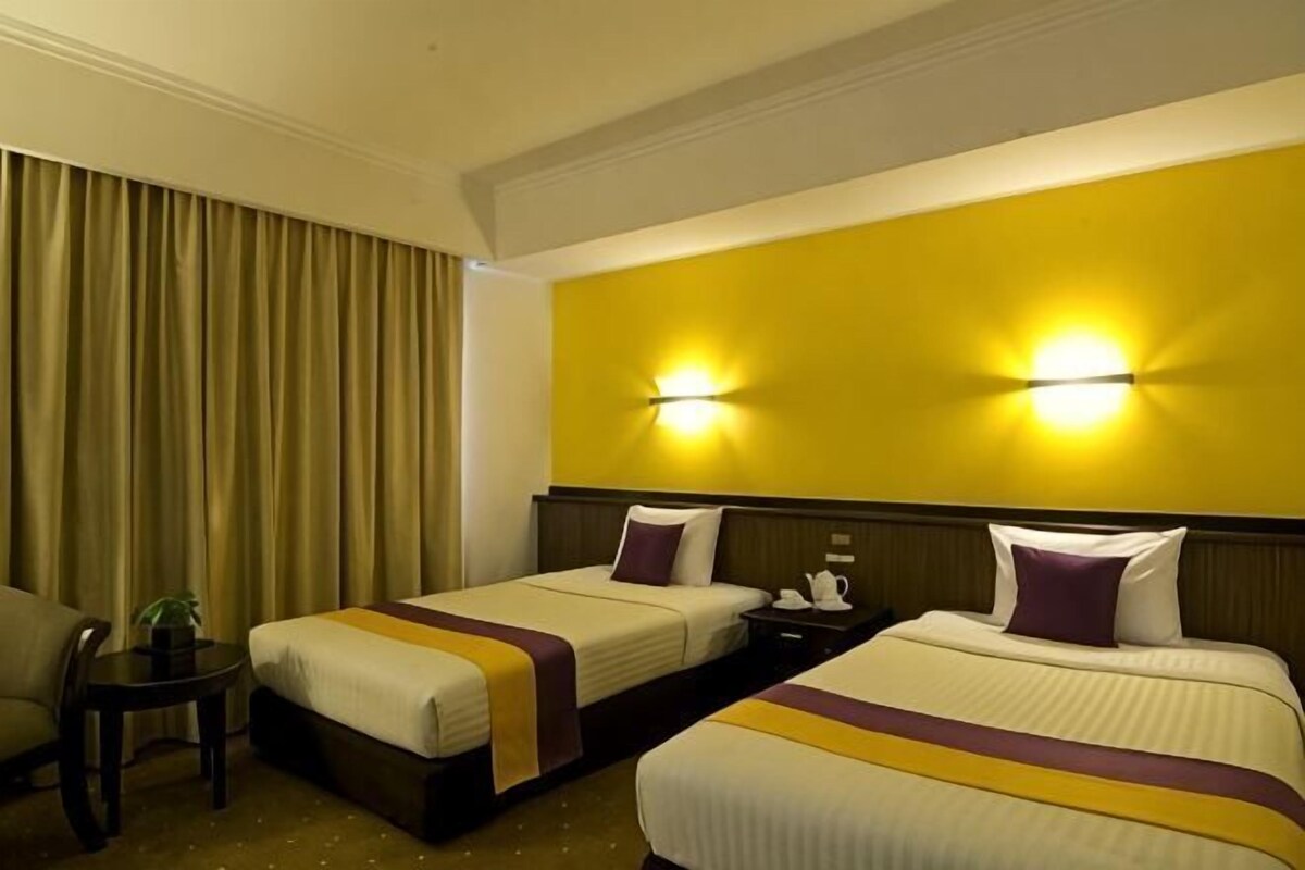 Habitación de hotel con dos camas, una mesita de noche, una silla y una lámpara.